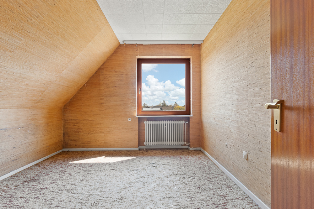 Leerer Raum mit Teppichboden, Holzvertäfelung und Fenster, durch das blauer Himmel zu sehen ist.