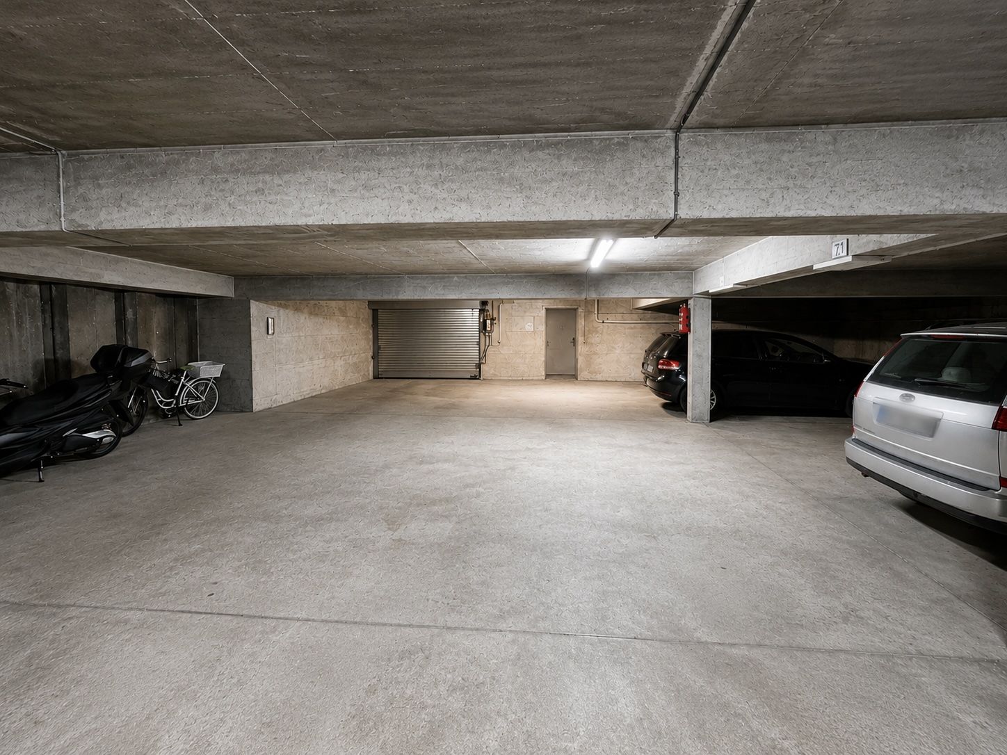 Tiefgaragenstellplatz mit Autos, Motorrädern und Fahrrädern, Betonwände und Decke.