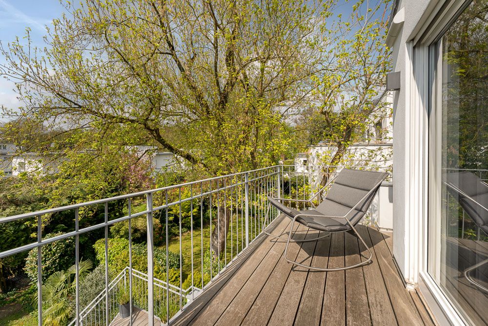 Balkon mit Holzfußboden, Stuhl und Blick auf grünen Garten mit Bäumen.
