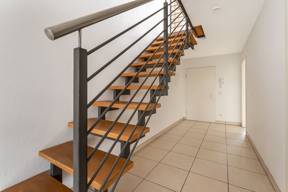 Flur mit gefliester Bodenfläche und moderner Treppe aus Holz und Metall.