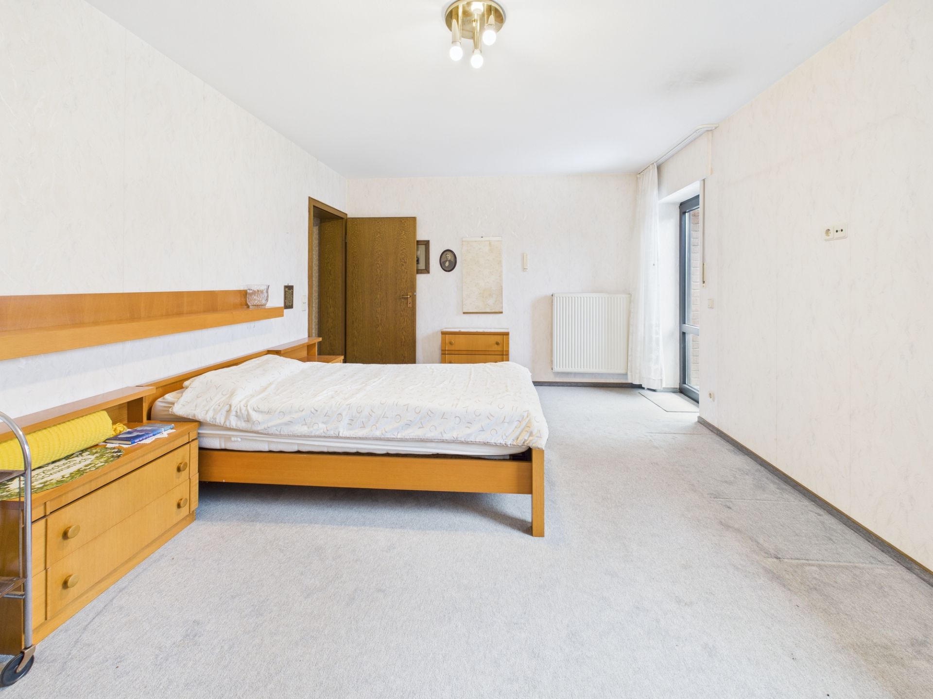 Helles Schlafzimmer mit Holzbett, Nachttisch und Zugang zu einem Balkon.