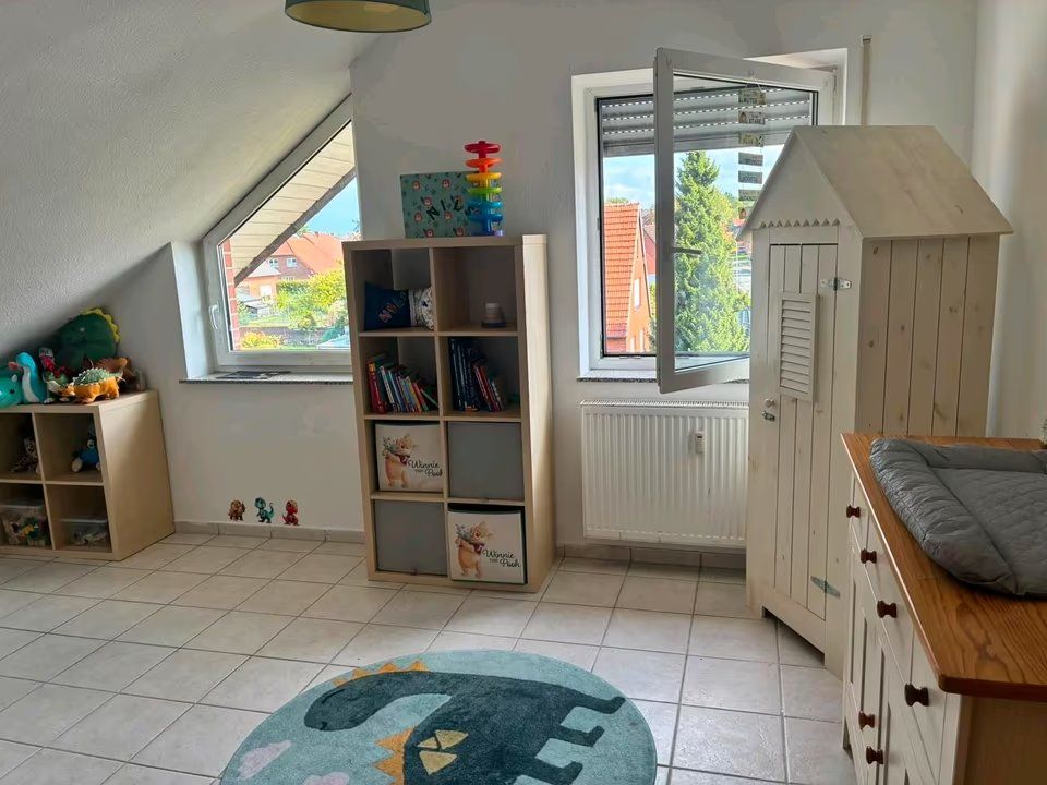 Helles Kinderzimmer mit Spielzeugregalen, Wickelkommode und einem Teppich mit Dinosauriermotiv.