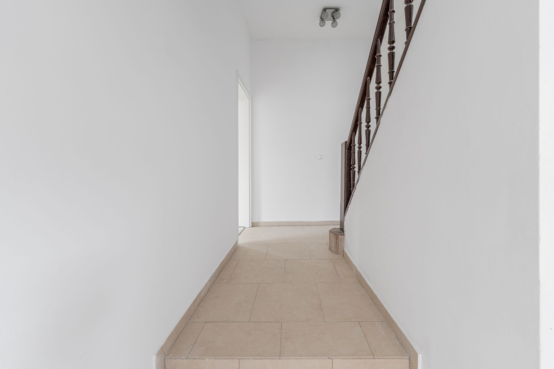 Heller Flur mit beiger Fliese und Treppe mit Holzgeländer auf der rechten Seite.