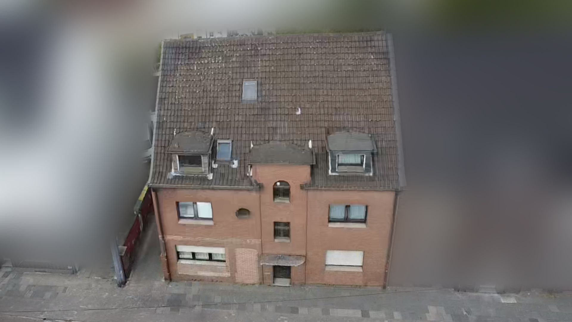 Dreistöckiges Backsteinhaus mit Satteldach und mehreren Fenstern, von vorne gesehen.