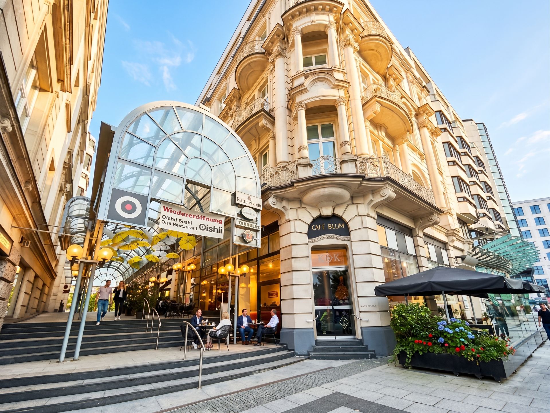 Ecke eines historischen Gebäudes mit großem Glasdach und Straßencafé, Menschen sitzen draußen.