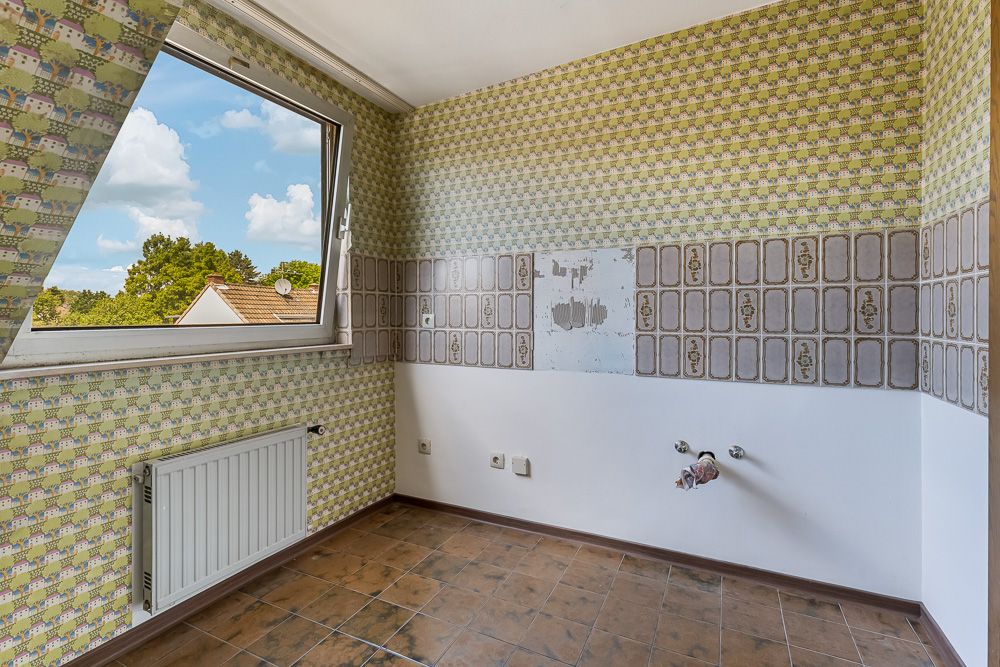 Leerer Raum mit gemusterter Tapete, geöffnetem Fenster und sichtbaren Wasseranschlüssen.