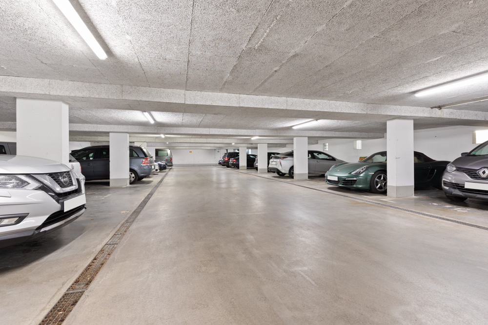 Helle Tiefgarage mit mehreren parkenden Autos und weißen Pfeilern.