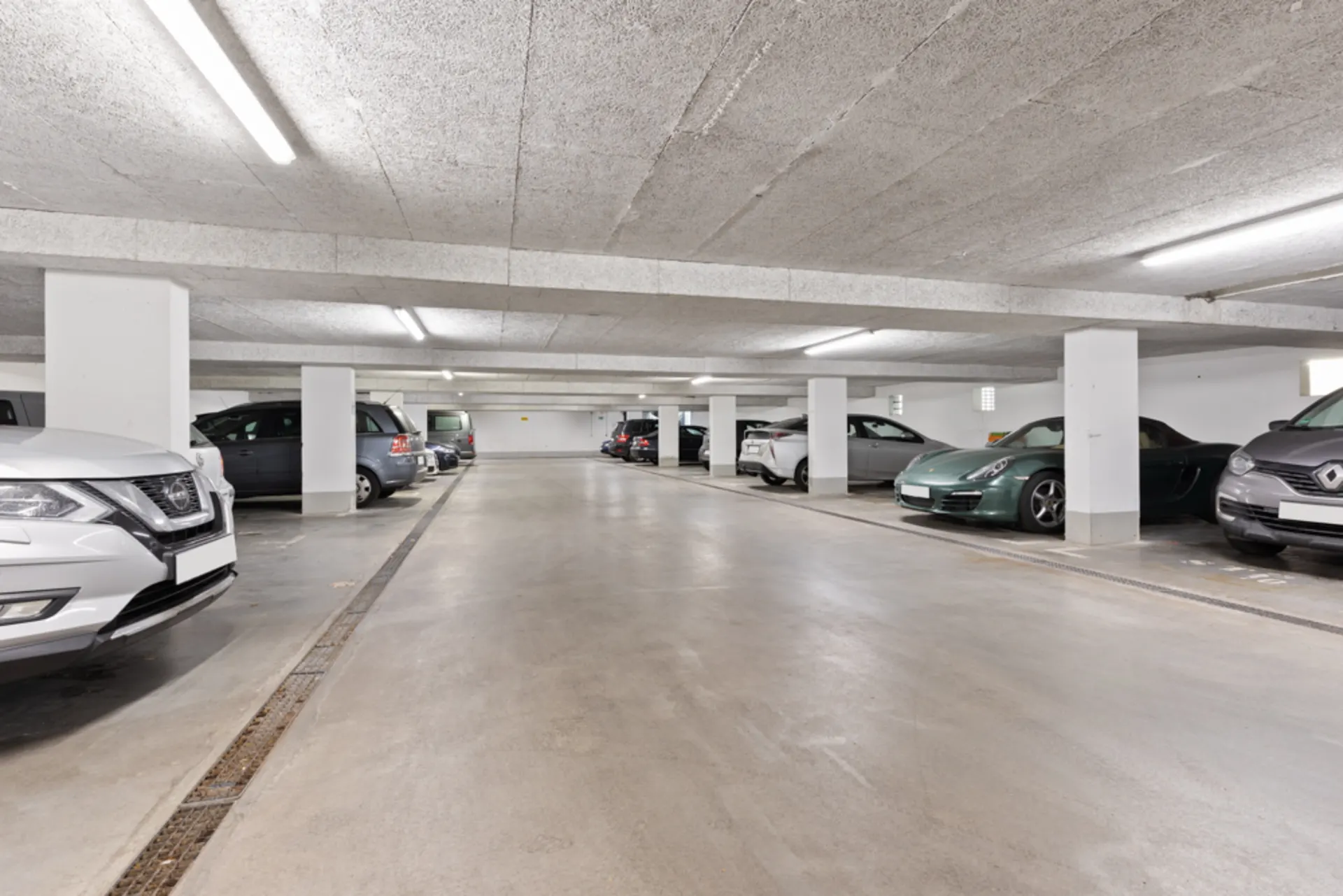 Helle Tiefgarage mit mehreren parkenden Autos und weißen Pfeilern.