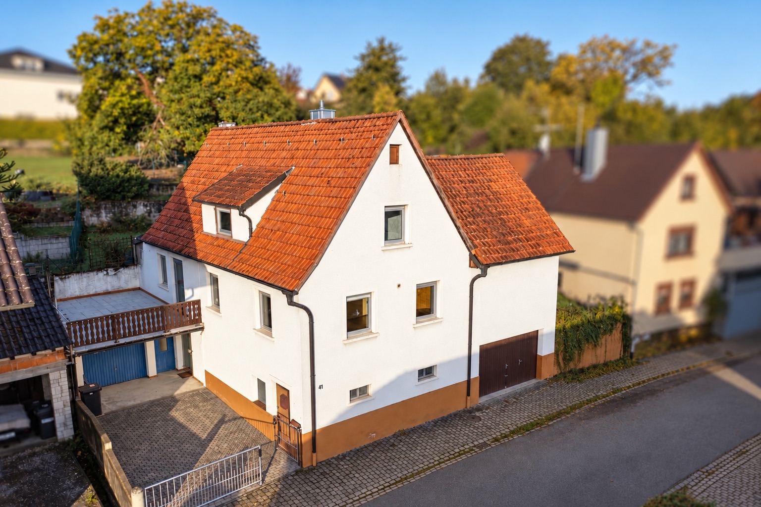 Weißes Wohnhaus mit rotem Satteldach an einer gepflasterten Straße.