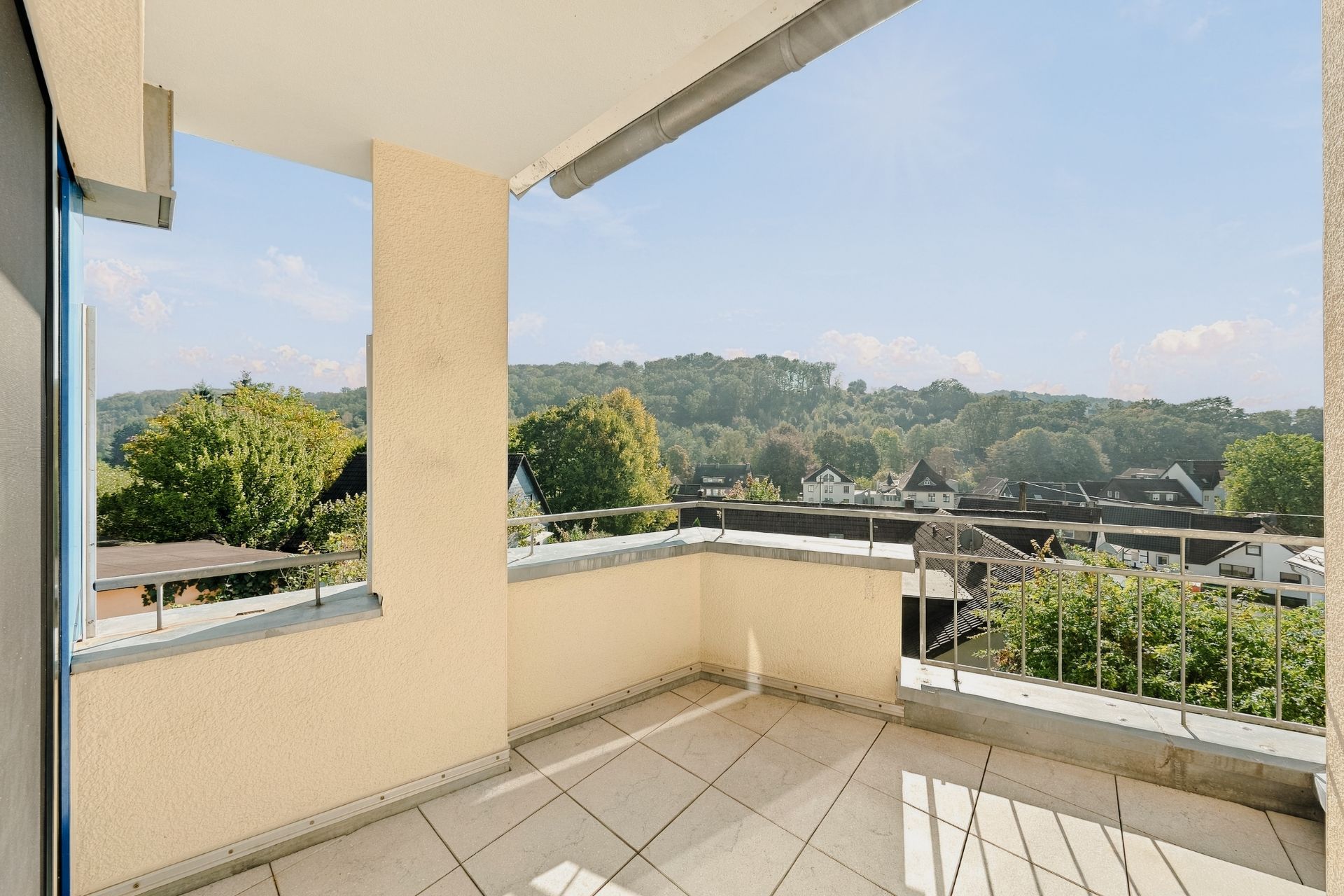 Balkon mit Fliesenboden und Blick auf Bäume und Häuser in einer Wohngegend.
