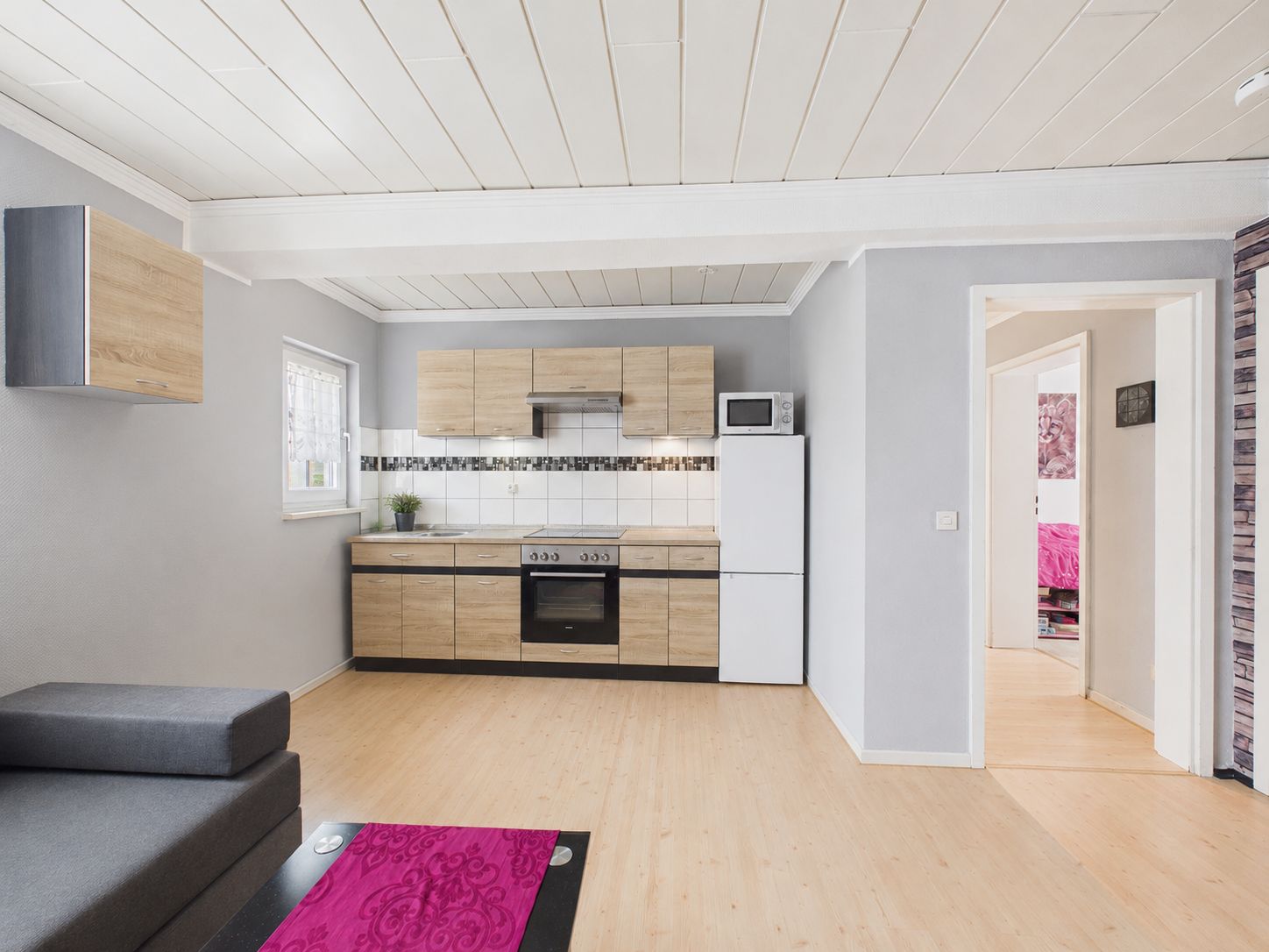 Moderne Einbauküche mit Holzfronten, Kühlschrank und Sofa in einem hellen Wohnraum.