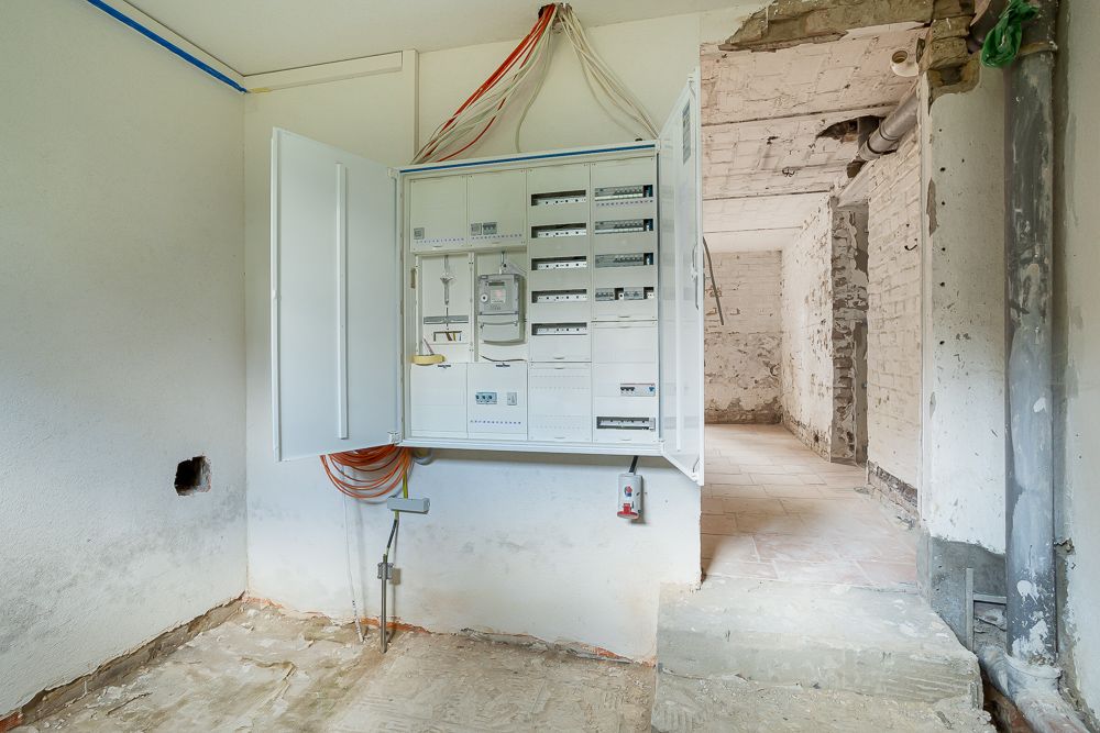 Offener Sicherungskasten mit Kabeln in einem Rohbau-Raum mit freiliegenden Wänden.