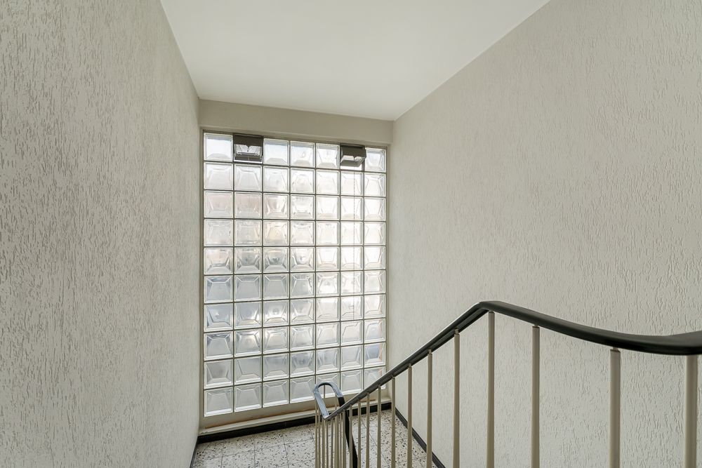 Treppenhaus mit Handlauf und großem Glasbausteinfenster.