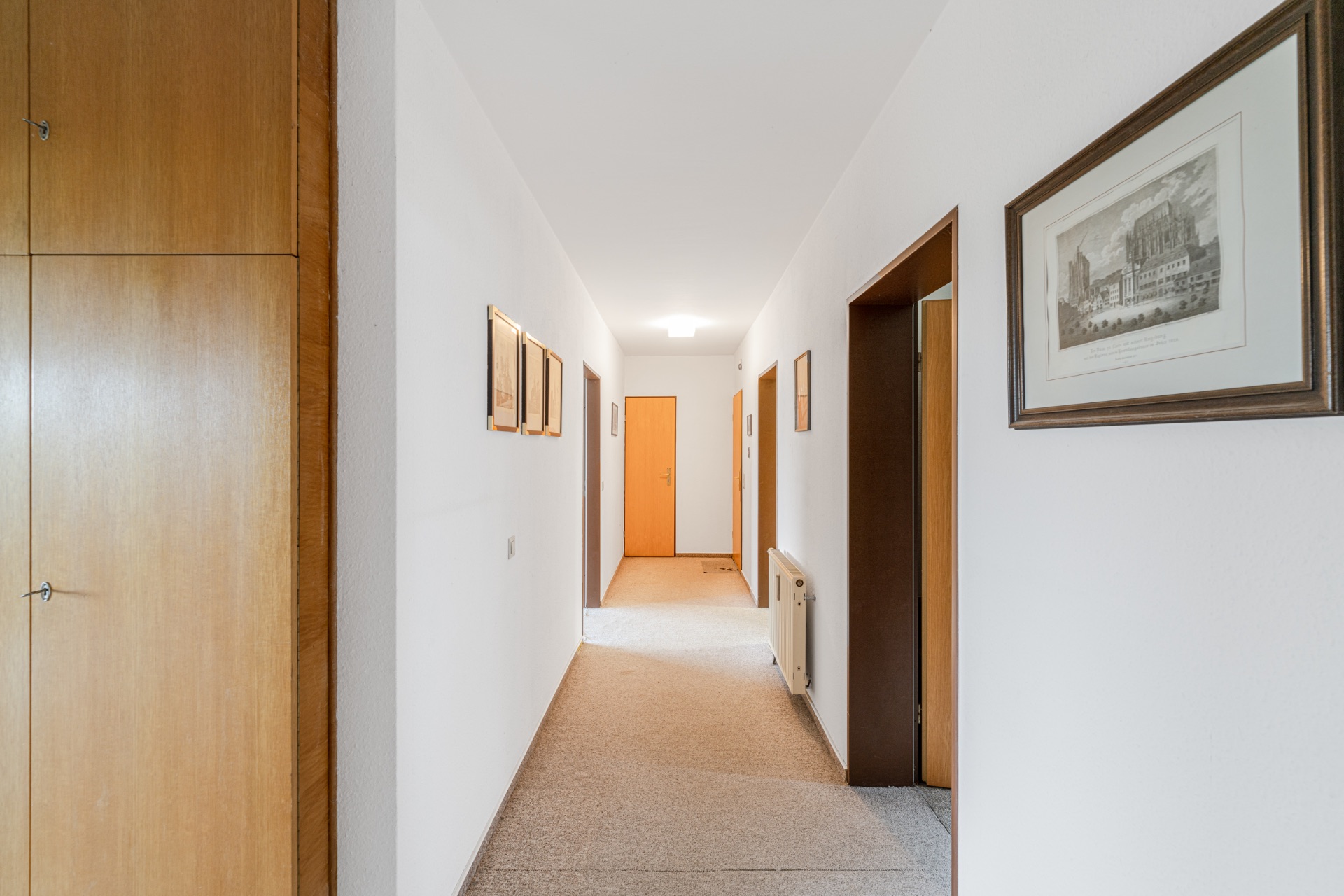 Heller Flur mit Teppich, Holztüren, weißen Wänden und gerahmten Bildern an den Wänden.