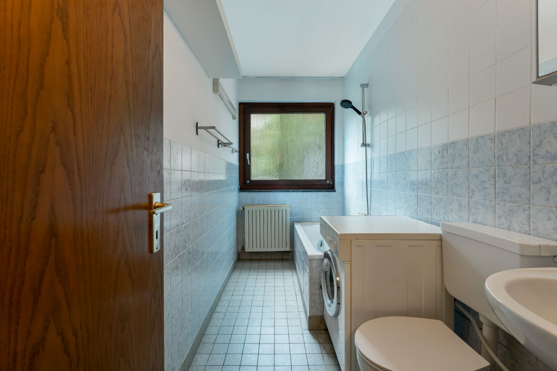 Schmales Badezimmer mit Waschmaschine, Toilette, Badewanne und Fenster.