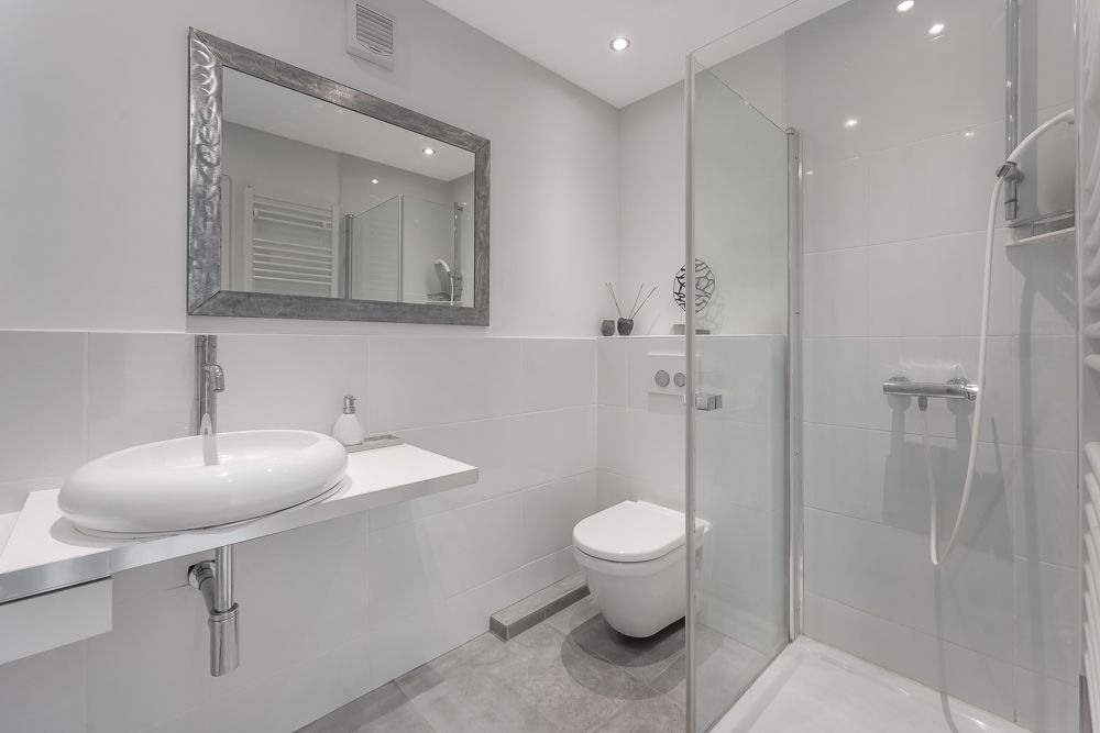 Modernes Badezimmer mit Waschbecken, Spiegel, Toilette und verglaster Dusche.
