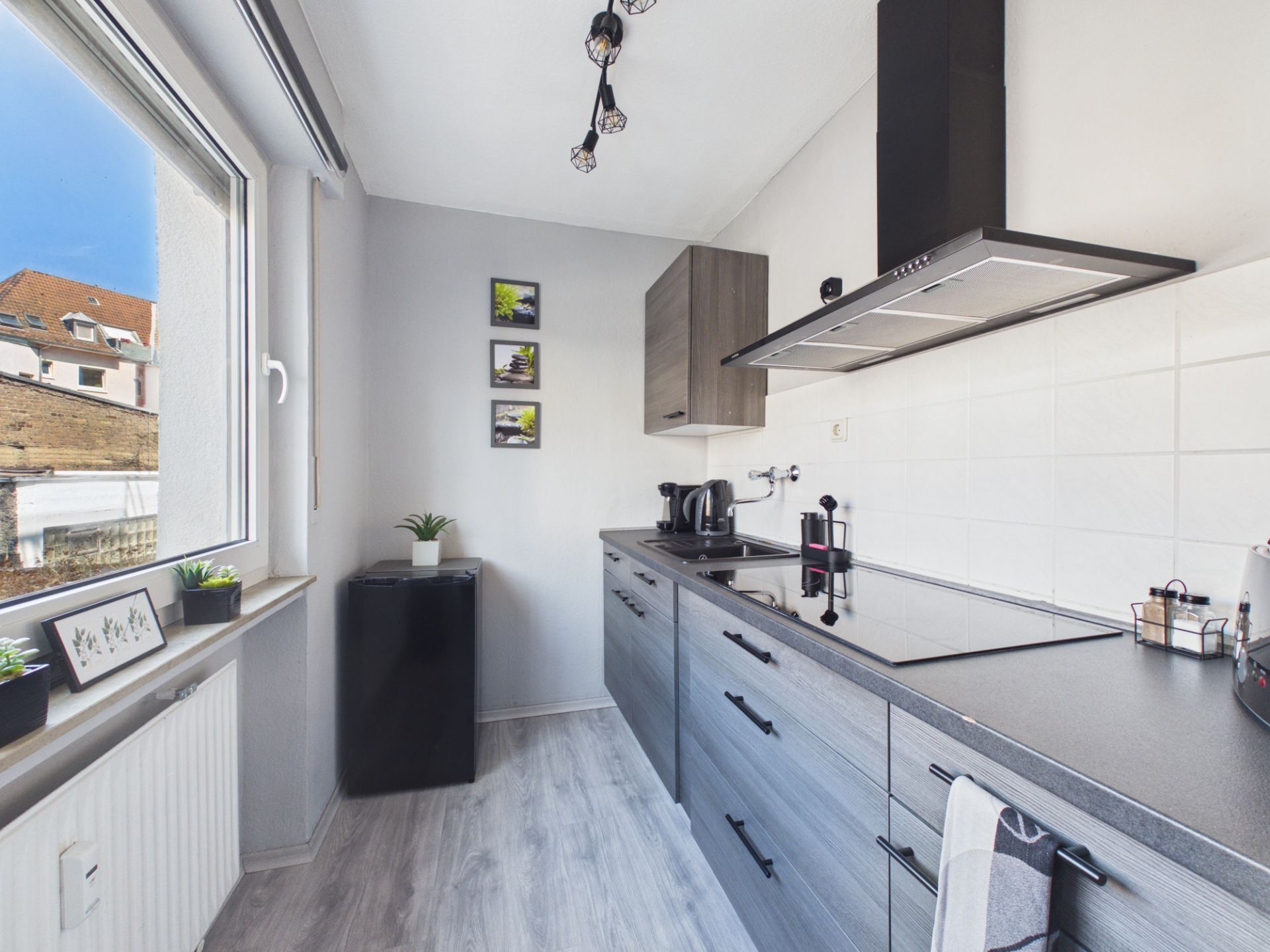 Moderne Küchenzeile mit Herd, Dunstabzugshaube und grauen Schränken, Fenster mit Pflanzen.