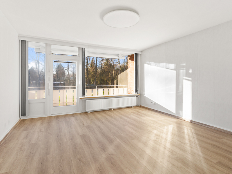 Helles, leeres Zimmer mit Holzboden, Balkon und großen Fenstern.