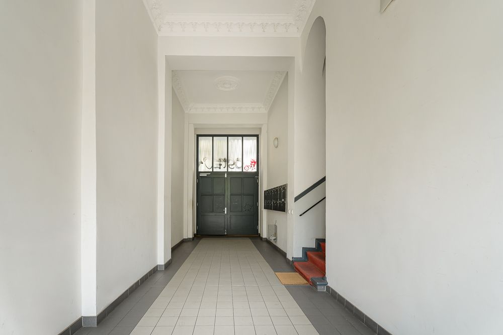 Heller Flur mit grauer Eingangstür, Briefkästen und Treppe mit rotem Teppich.