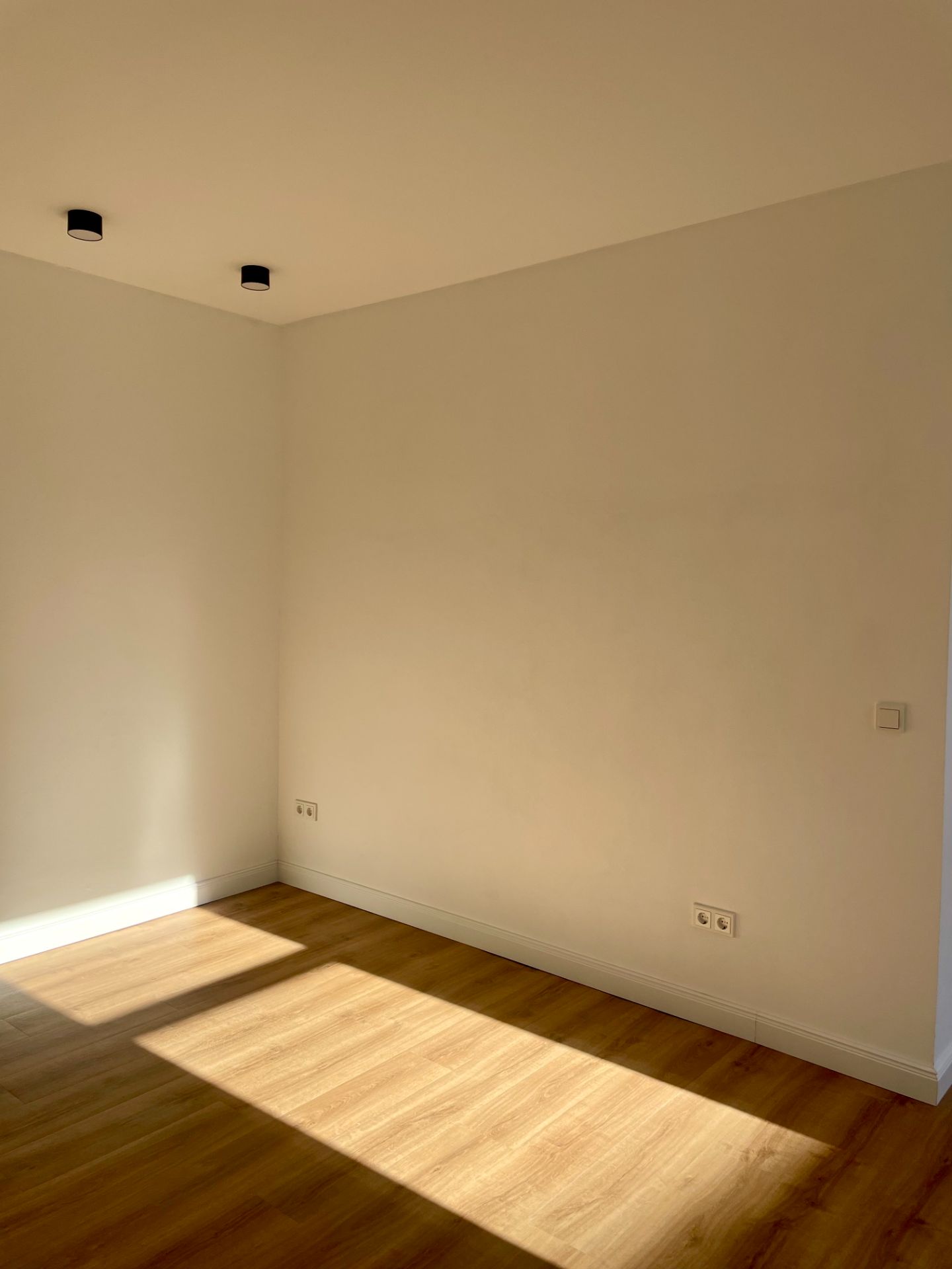 Leerer Raum mit Holzfußboden, weißen Wänden und Sonnenlicht auf dem Boden.