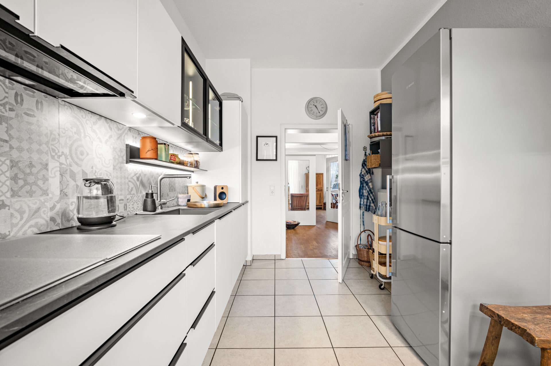 Moderne Küche mit weißen Schränken, großem Kühlschrank und Blick ins angrenzende Wohnzimmer.