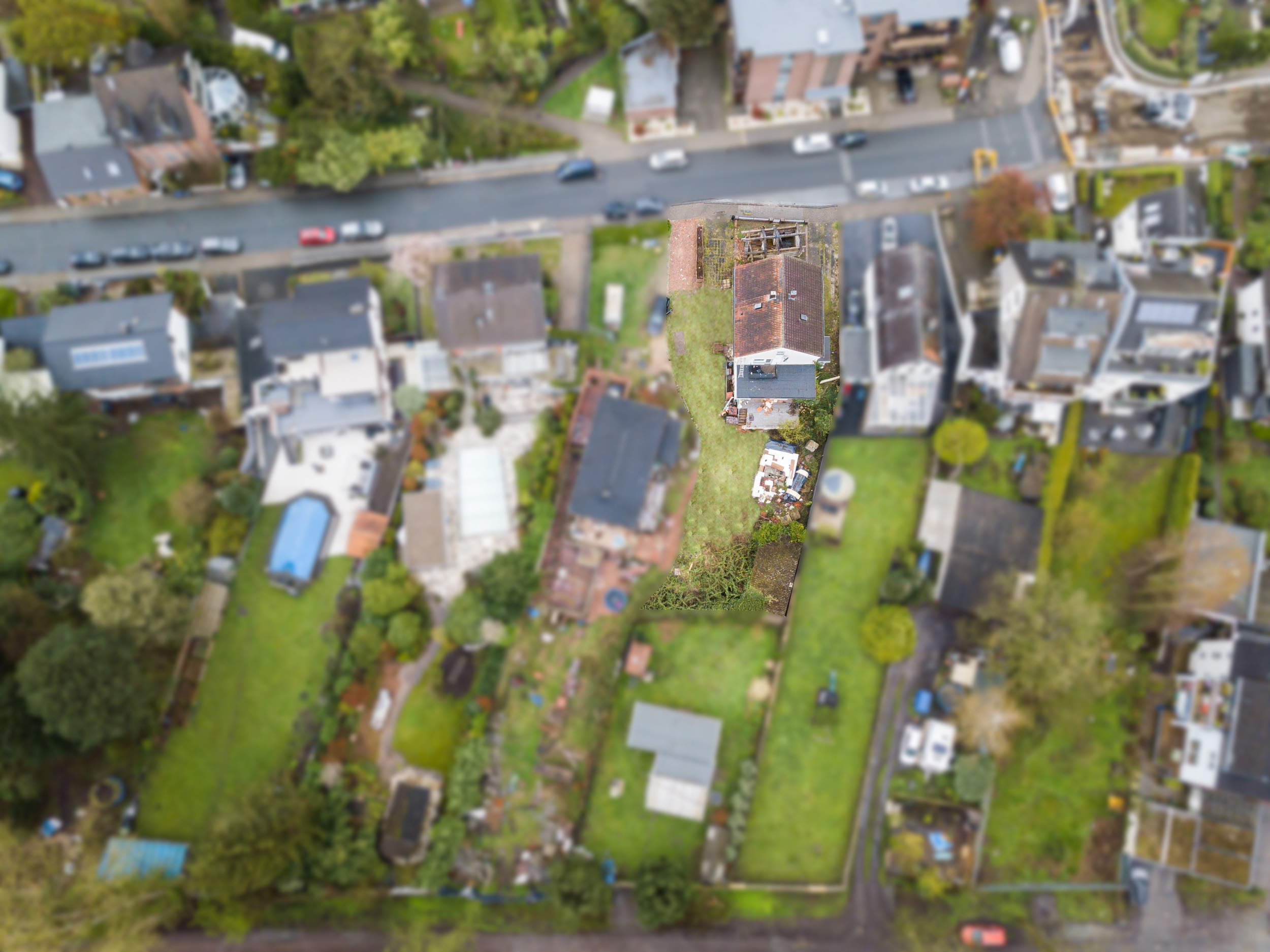Vogelperspektive auf Wohnhäuser mit Gärten und einer Straße im Vordergrund.