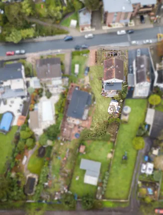 Vogelperspektive auf Wohnhäuser mit Gärten und einer Straße im Vordergrund.