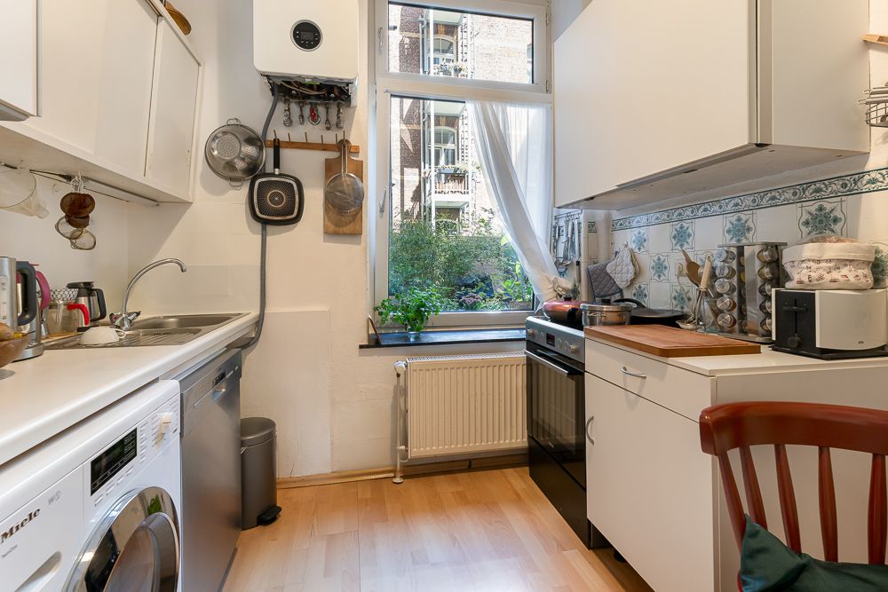 Helle Küche mit Waschmaschine, Herd, Spüle, weißen Schränken und Fenster mit Ausblick.