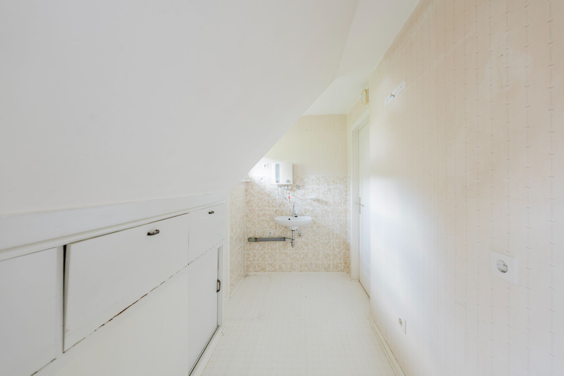 Heller, schmaler Raum mit Dachschräge, Waschbecken und Einbauschrank.