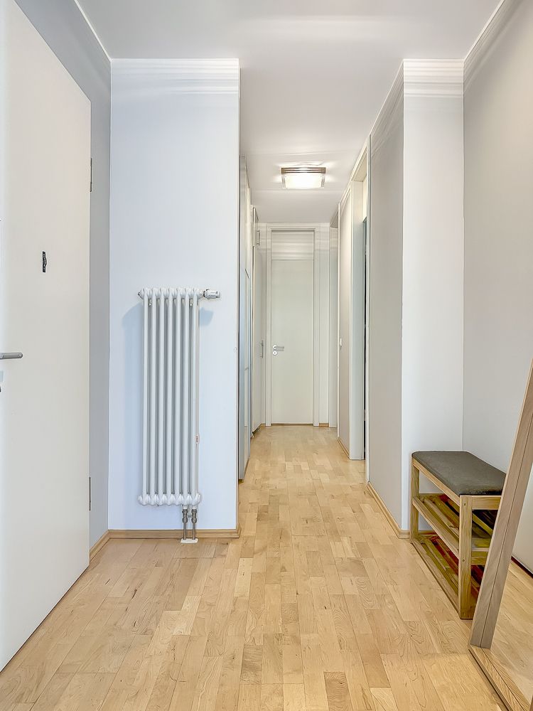 Heller Flur mit Holzboden, Heizkörper, Bank und Spiegel an der Wand.