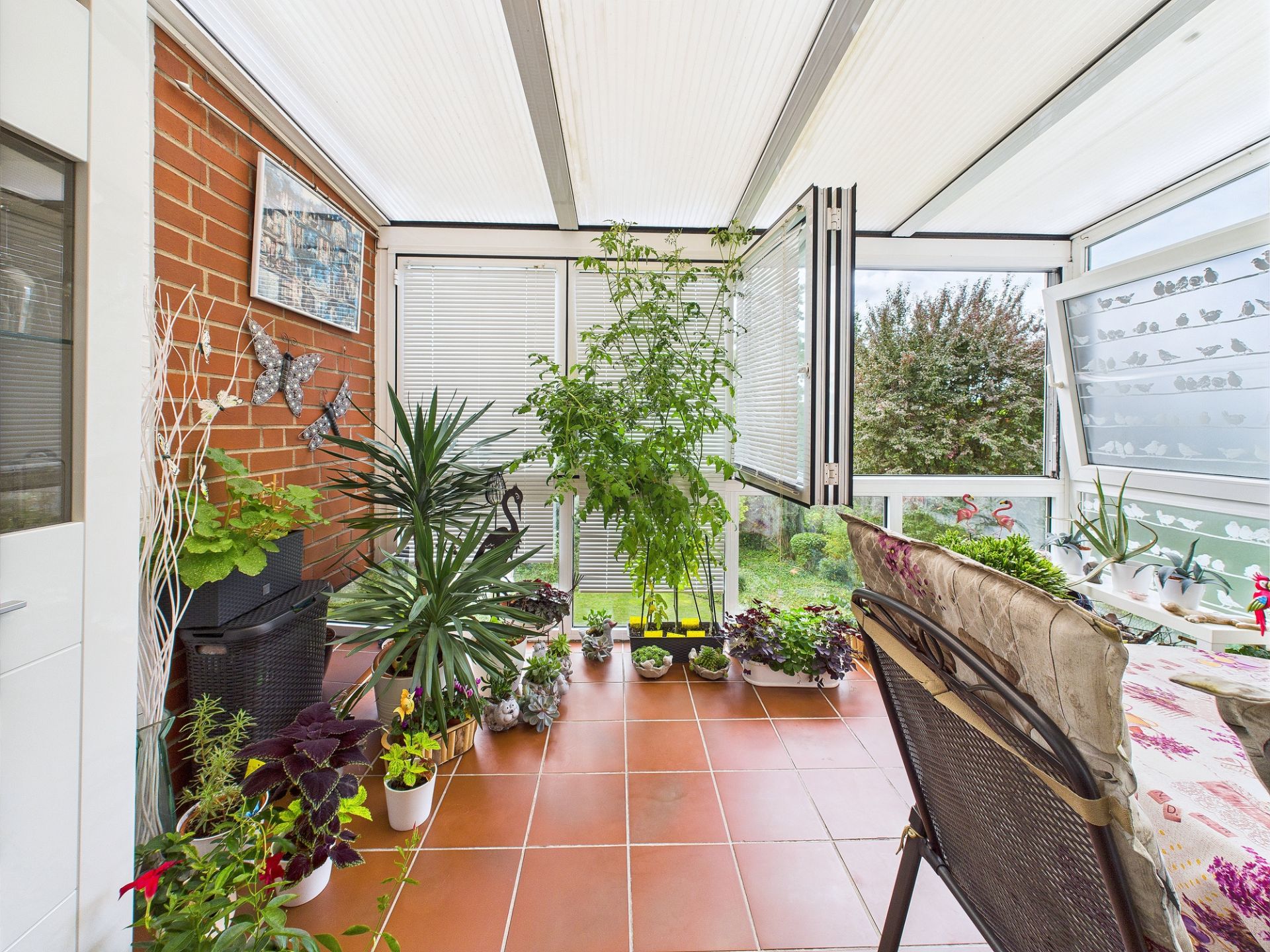 Heller Wintergarten mit vielen Topfpflanzen und Terrakottafliesen.