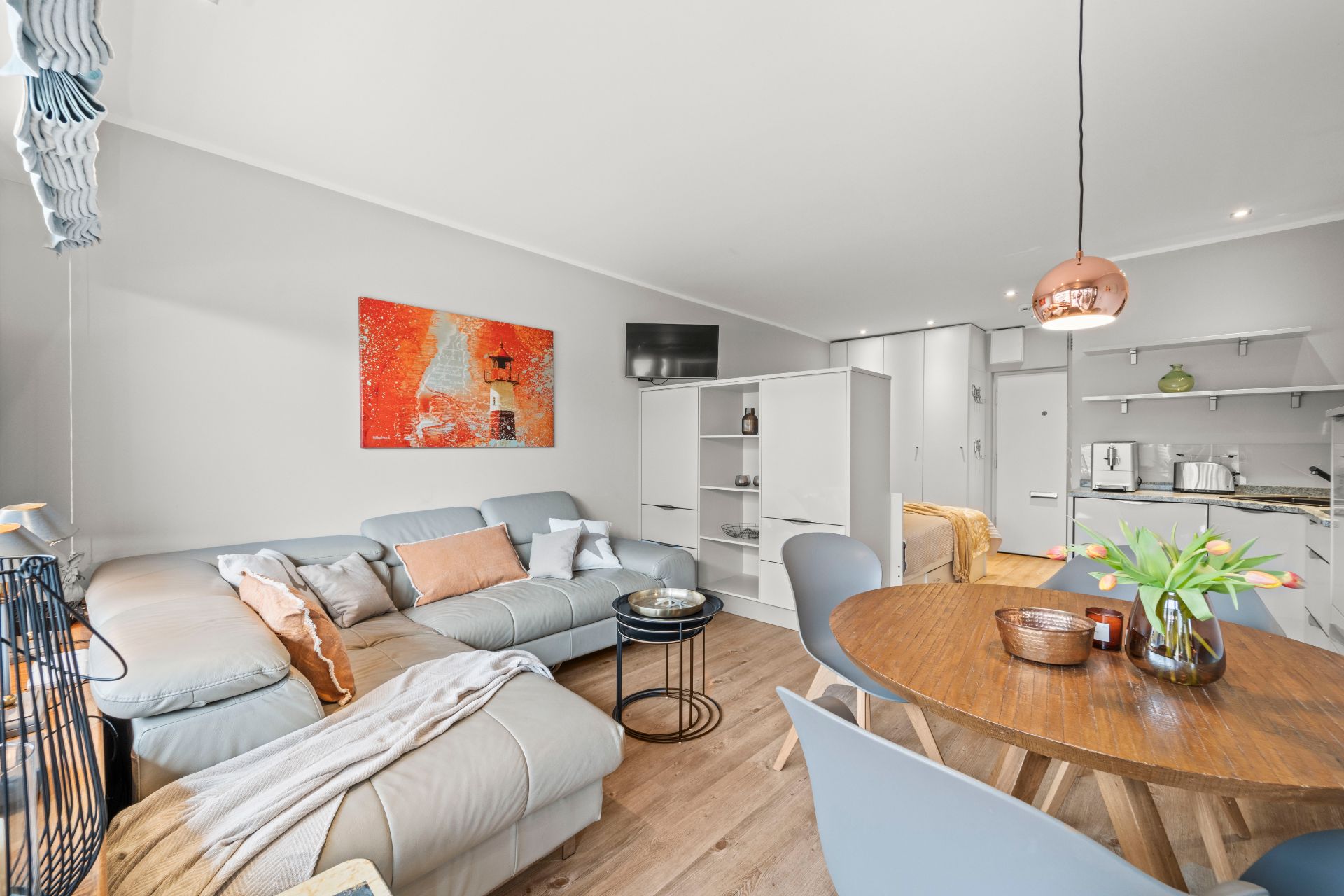 Modernes Wohnzimmer mit Sofa, rundem Esstisch, offener Küche und Wandbild.