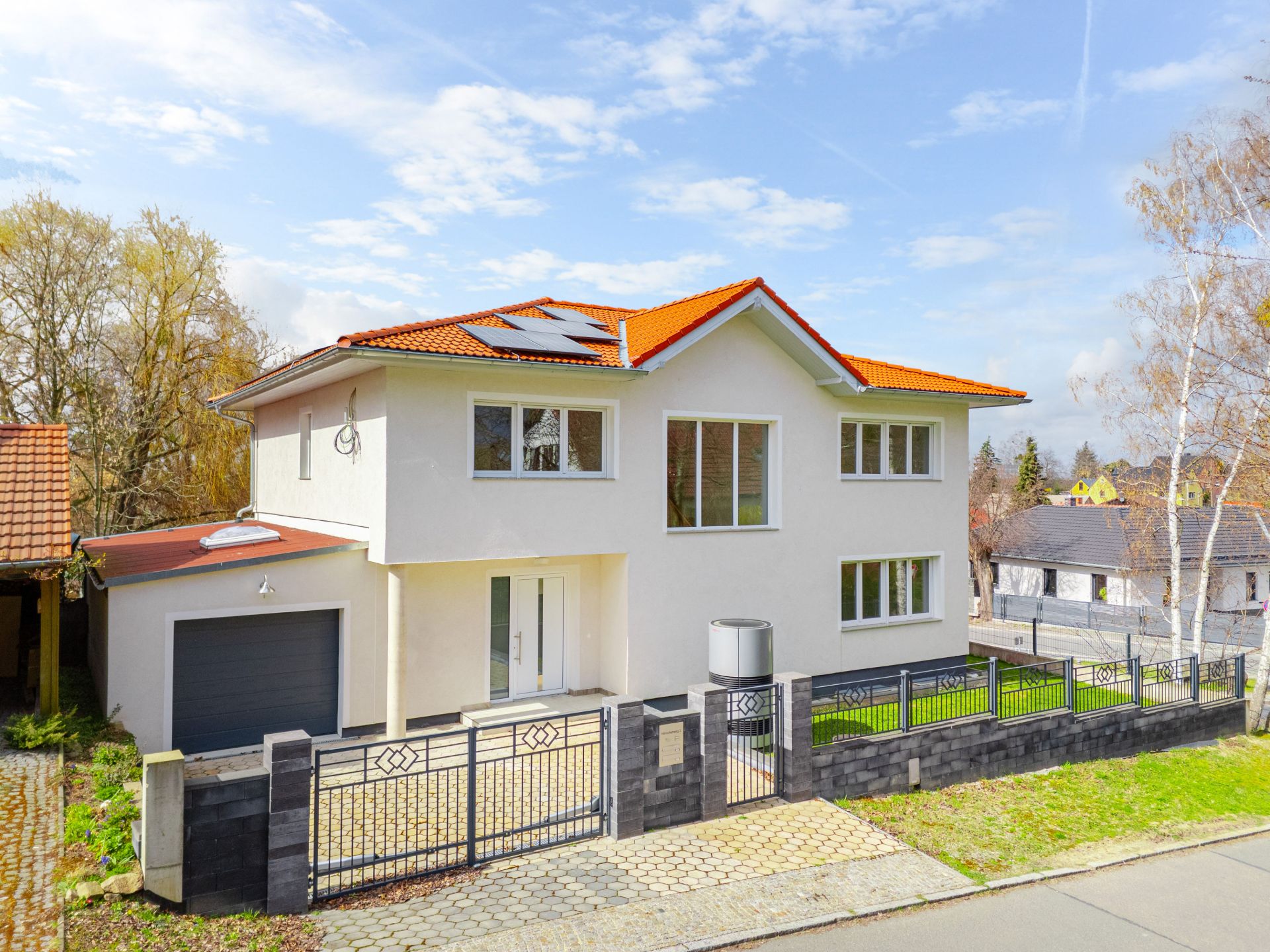 Modernes, zweistöckiges weißes Haus mit rotem Dach und Garage, von Zaun umgeben.