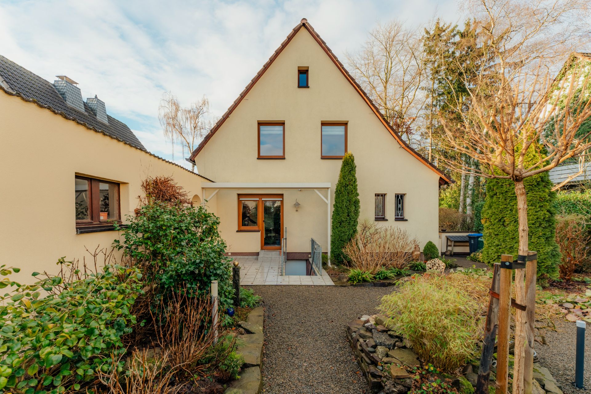 Zweistöckiges Haus mit Satteldach, Gartenweg und winterlichen Pflanzen im Vorgarten.