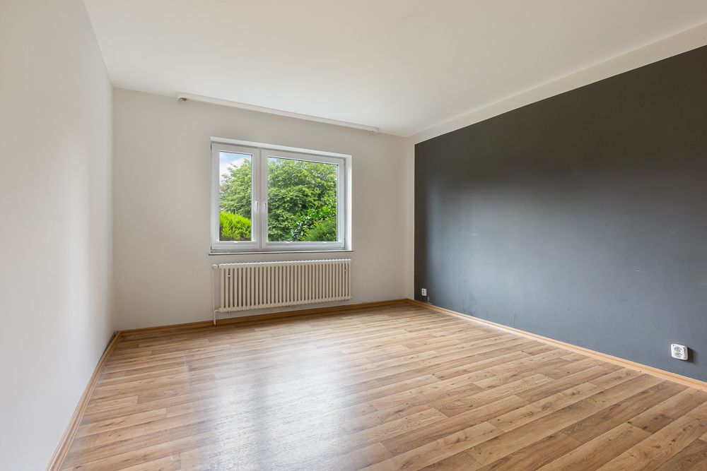 Leerer Raum mit Holzfußboden, Fenster und dunkelgrauer Akzentwand.