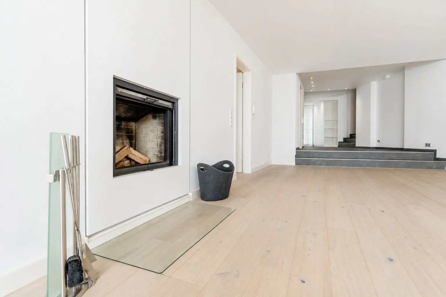 Helles Wohnzimmer mit Kamin, Holzboden und Treppen zu einem erhöhten Bereich.