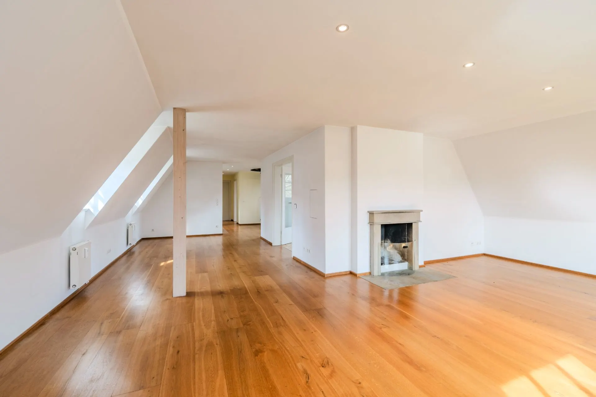 Helles Wohnzimmer mit Holzfußboden, Kamin und Dachschrägen.