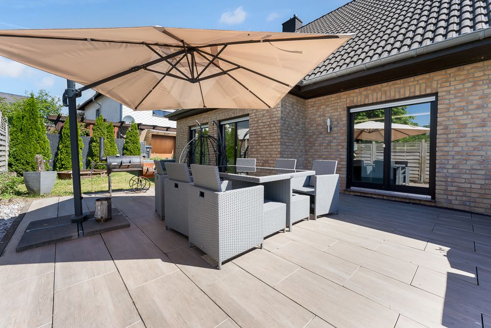 Moderne Terrasse mit Esstisch, Stühlen und großem Sonnenschirm vor einem Backsteinhaus.