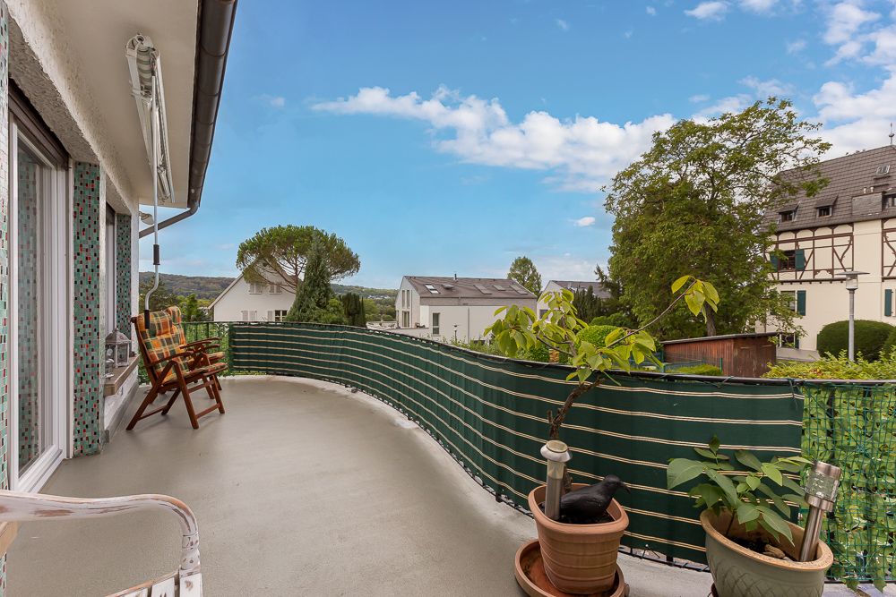 Balkon mit Stühlen, Pflanzen in Töpfen und Blick auf Nachbarhäuser unter blauem Himmel.