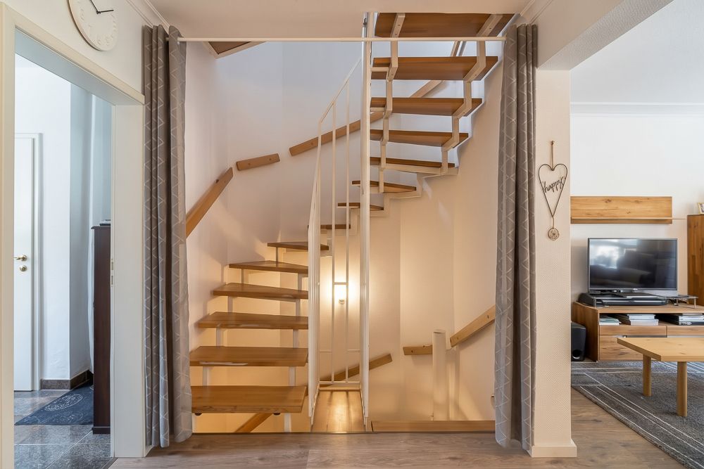 Holztreppe mit weißen Geländern in einem Wohnzimmer mit Fernseher und Couchtisch.