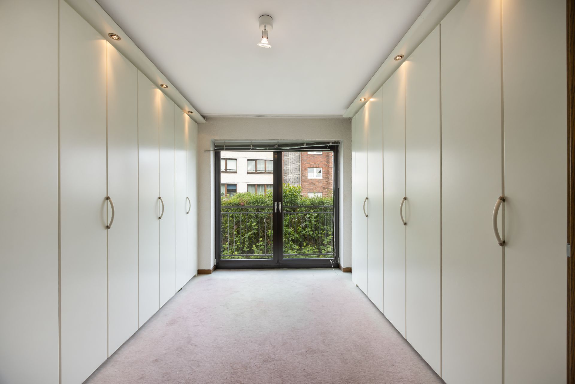 Heller Raum mit weißen Einbauschränken auf beiden Seiten und Glas-Doppeltür zum Balkon.