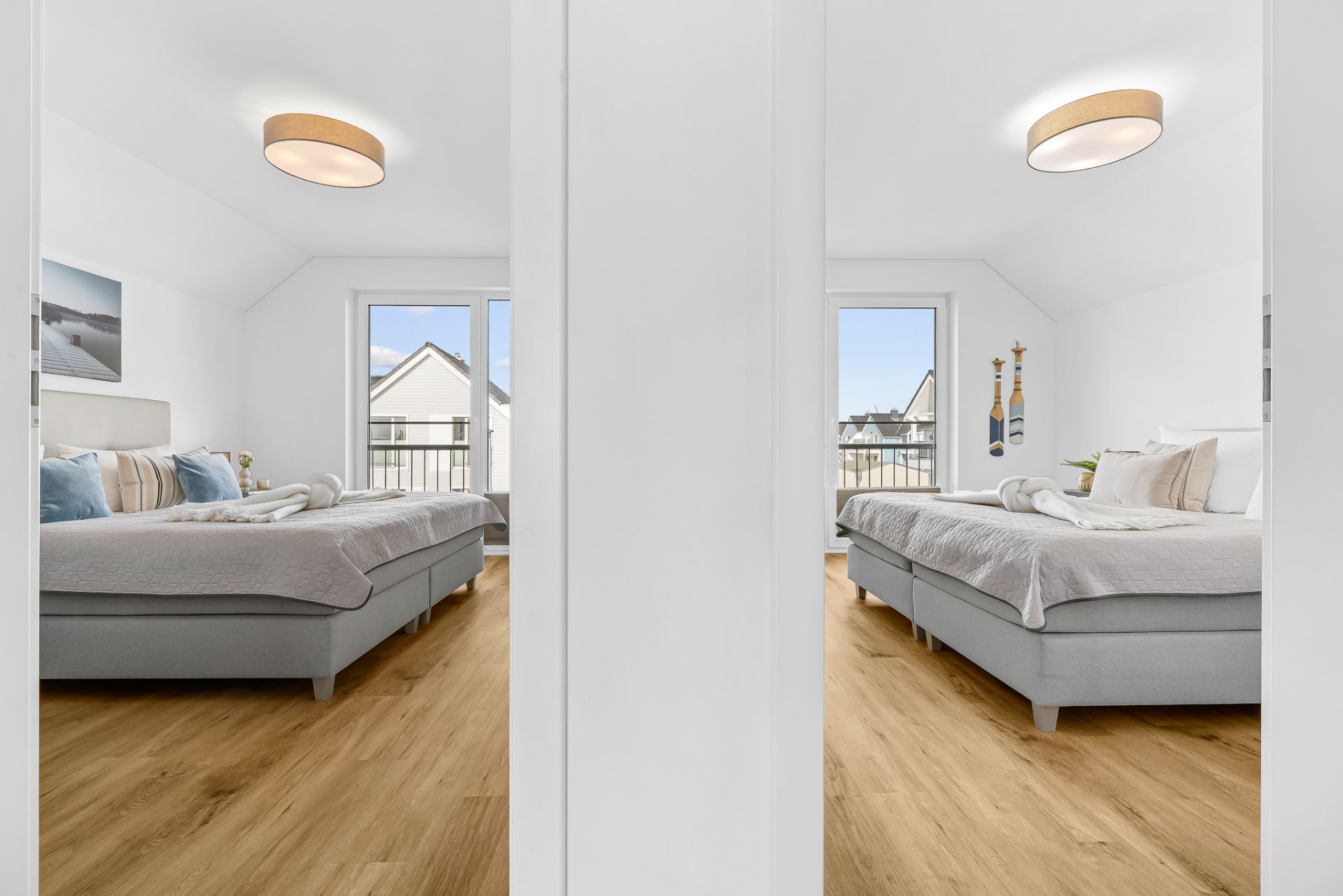 Helles Schlafzimmer mit zwei grauen Betten, Holzboden und großen Fenstern, gespiegelt im Schrank.