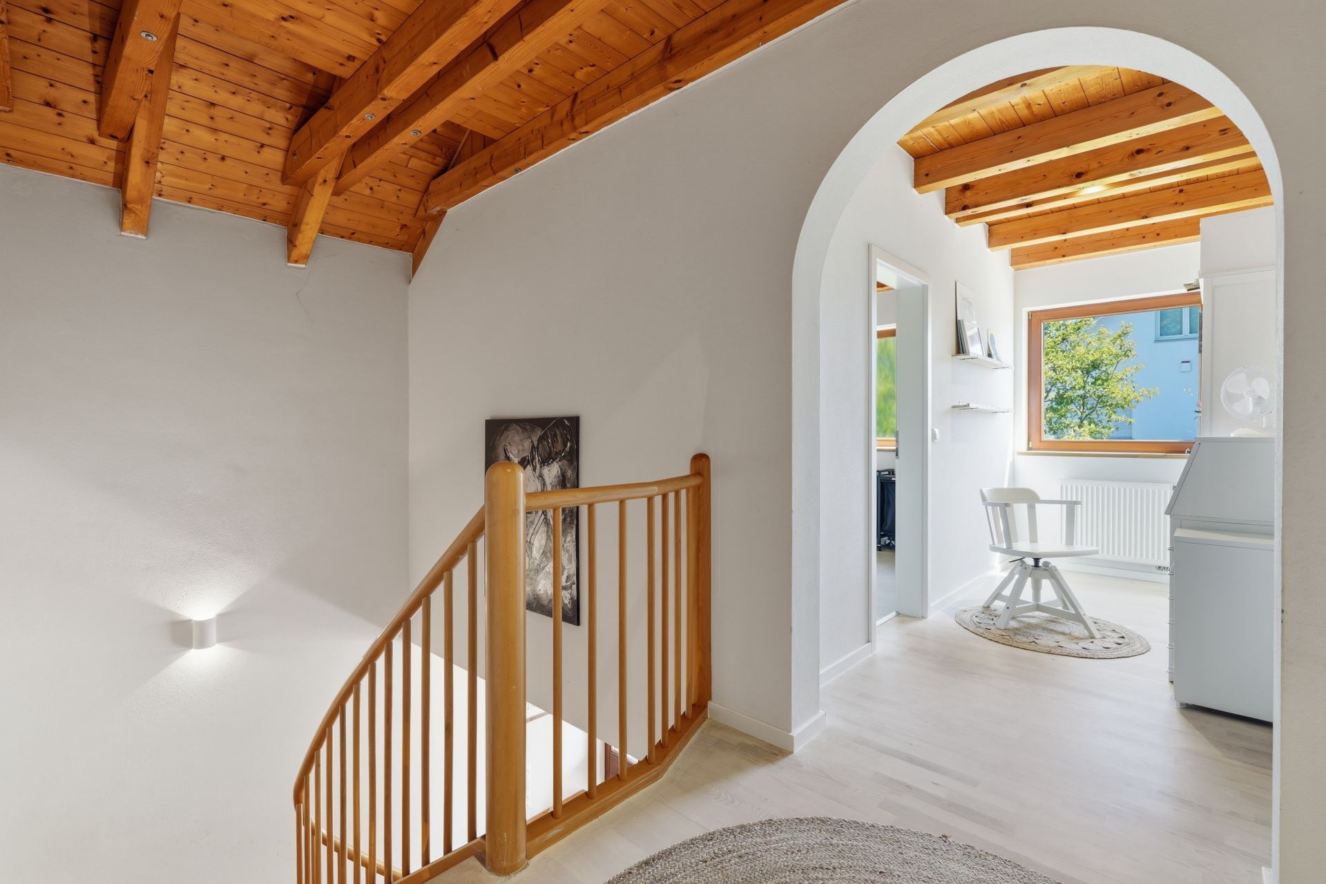 Heller Flur mit Holzdecke, Treppe, Rundbogen und Blick in ein Zimmer mit Holzstuhl.