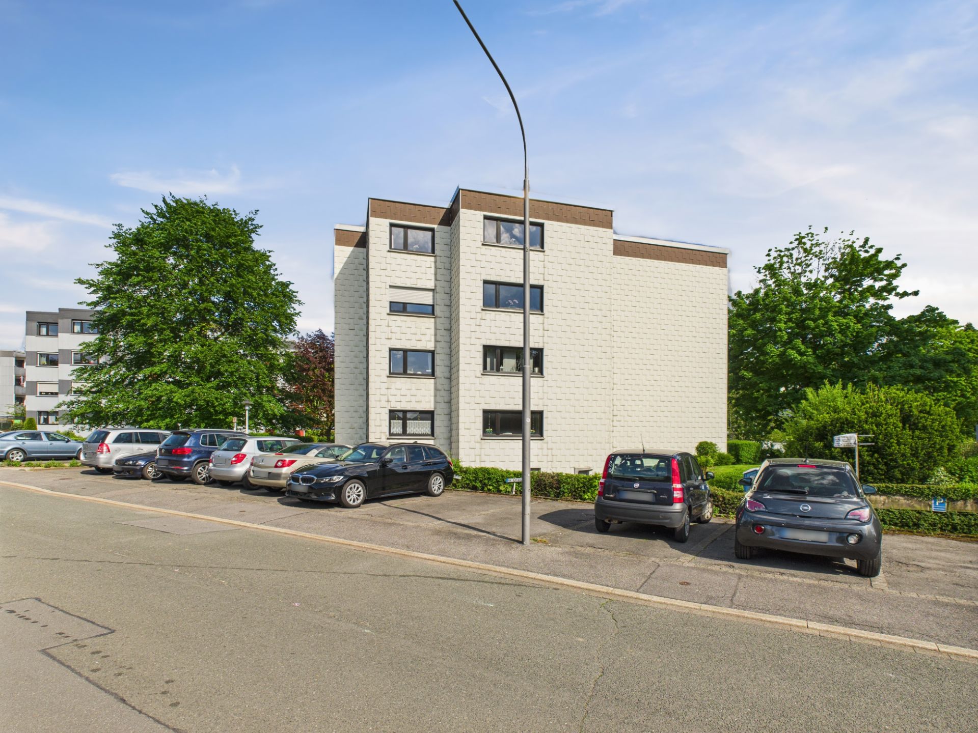 Mehrfamilienhaus mit mehreren geparkten Autos davor und Bäumen im Hintergrund.