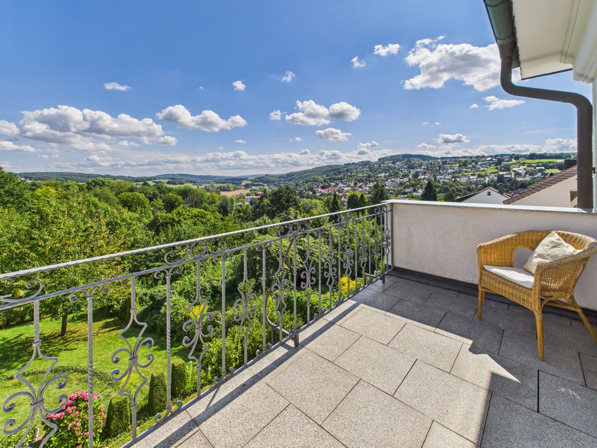 Balkon mit Stuhl und Kissen, Ausblick auf grüne Landschaft und Häuser im Hintergrund.