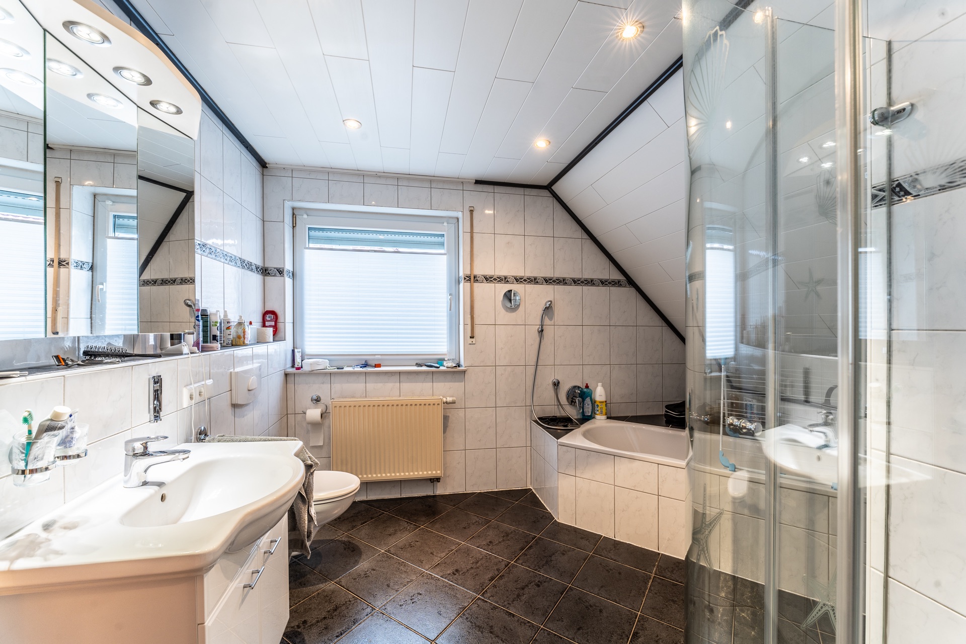 Modernes Badezimmer mit Waschbecken, Toilette, Eckbadewanne und Dusche unter Dachschräge.