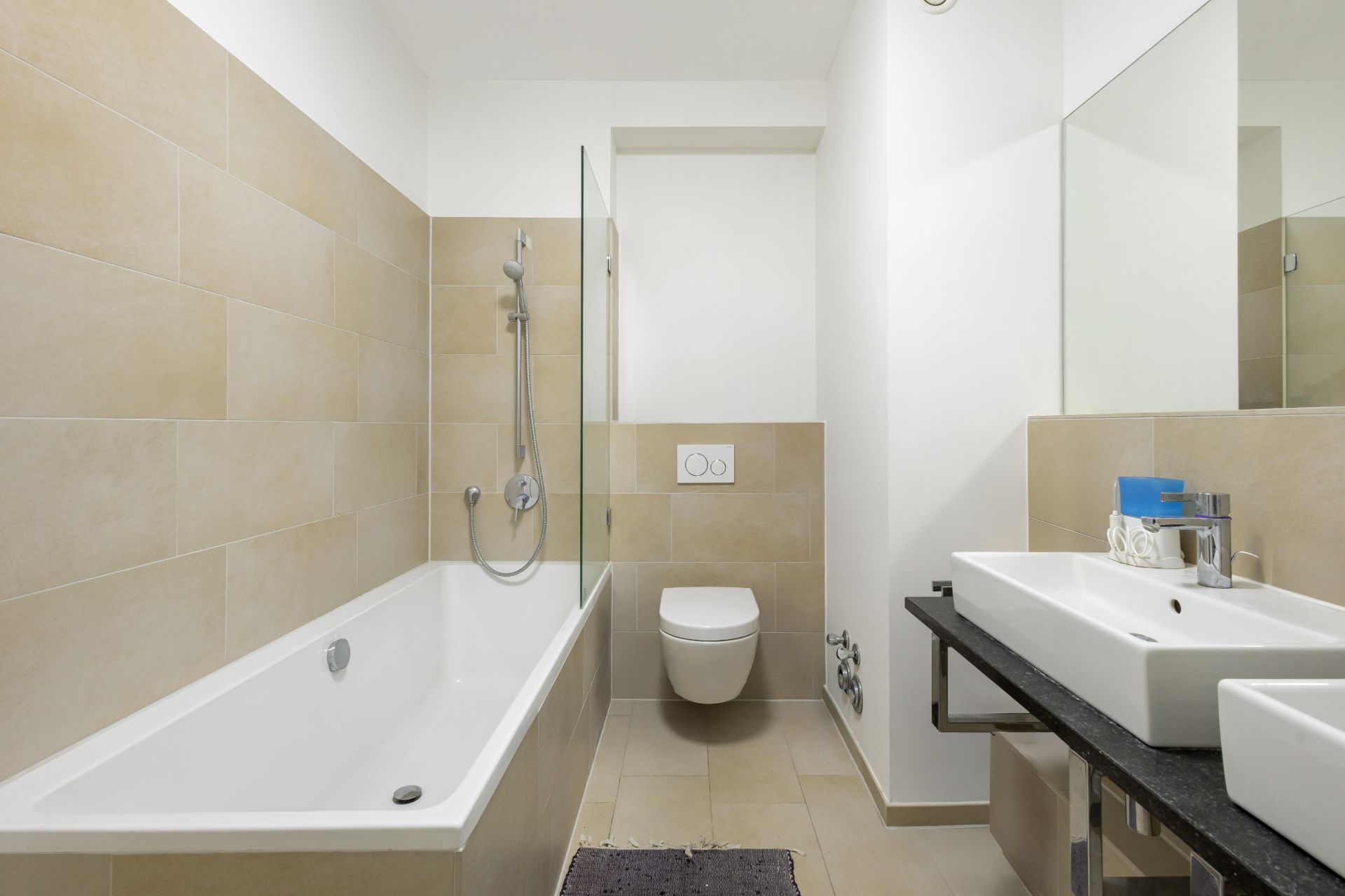 Modernes Badezimmer mit Badewanne, Wandtoilette und zwei Waschbecken.
