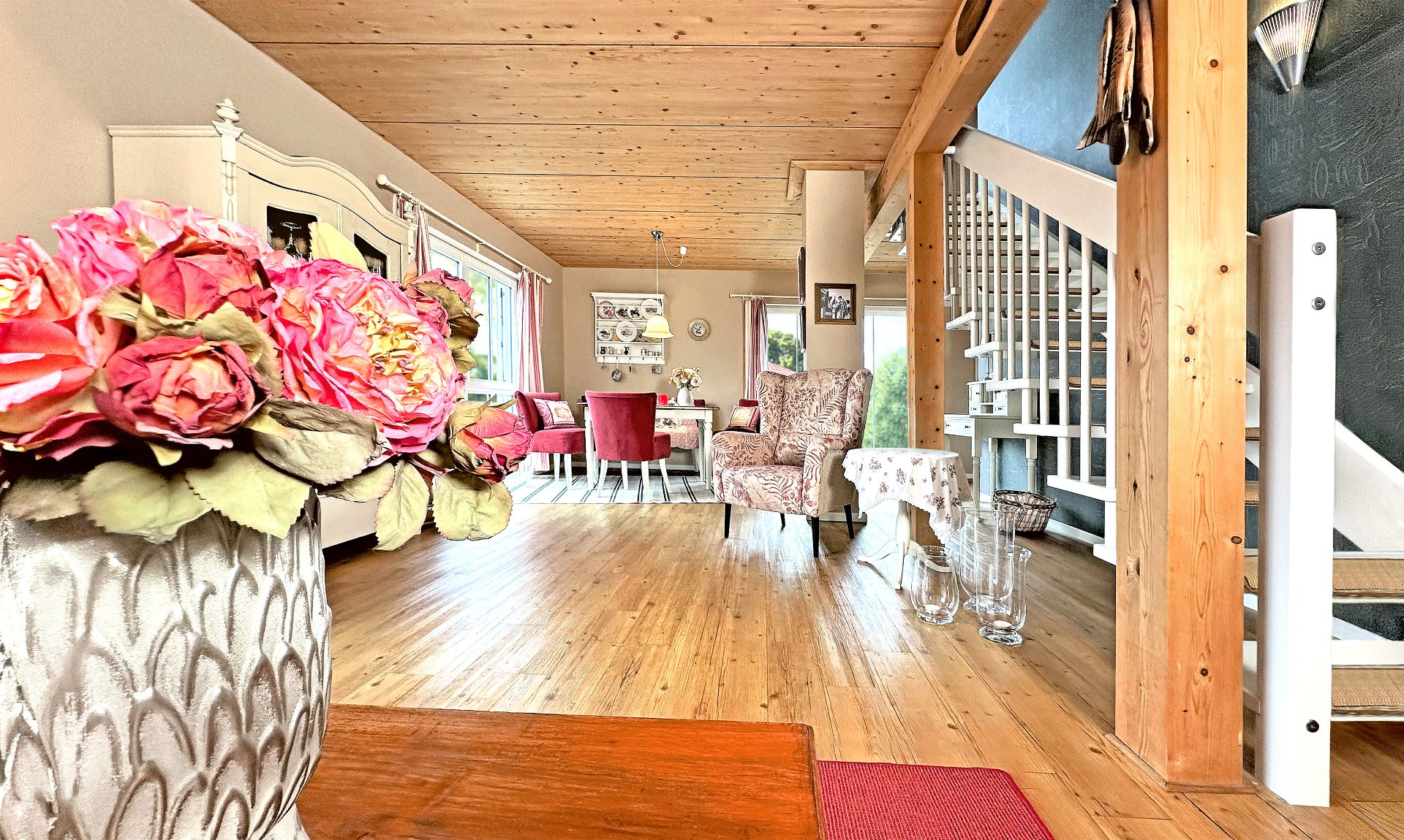 Helles Wohnzimmer mit Holzboden, Blumen, Esstisch, Sesseln und Treppe.