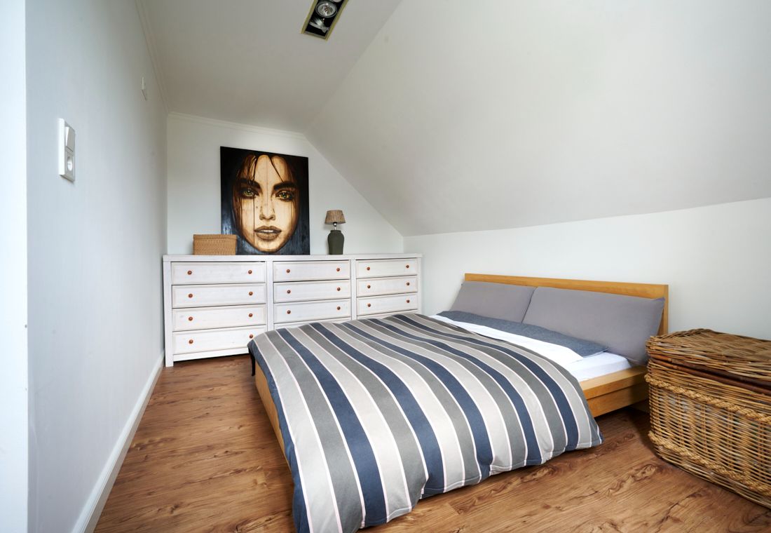 Schlafzimmer mit Doppelbett, gestreifter Bettdecke, weißer Kommode und Wandbild unter Dachschräge.