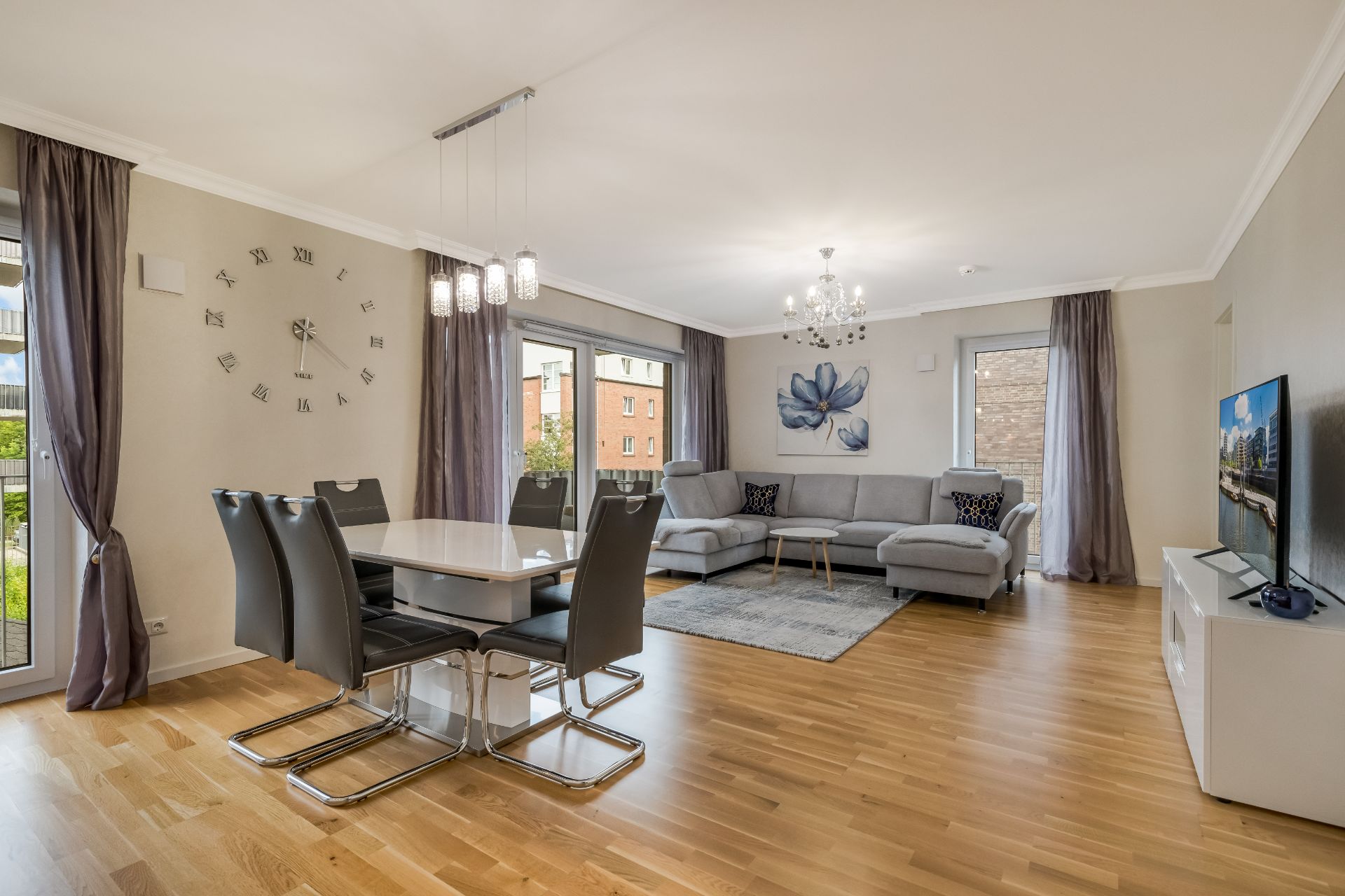 Modernes Wohnzimmer mit grauem Sofa, Esstisch, Stühlen, Fernseher und Holzboden.
